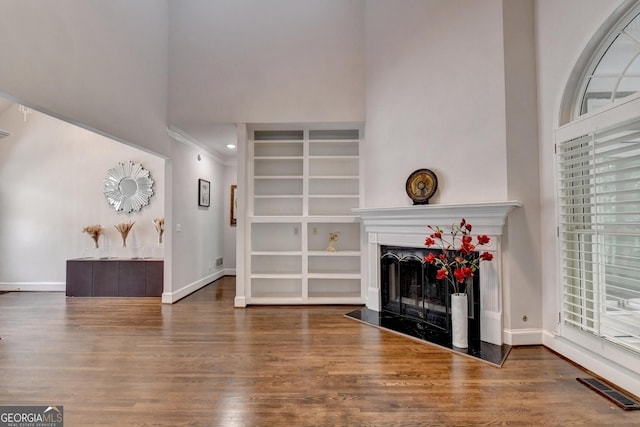 living room with visible vents, a fireplace with raised hearth, baseboards, a high ceiling, and wood finished floors