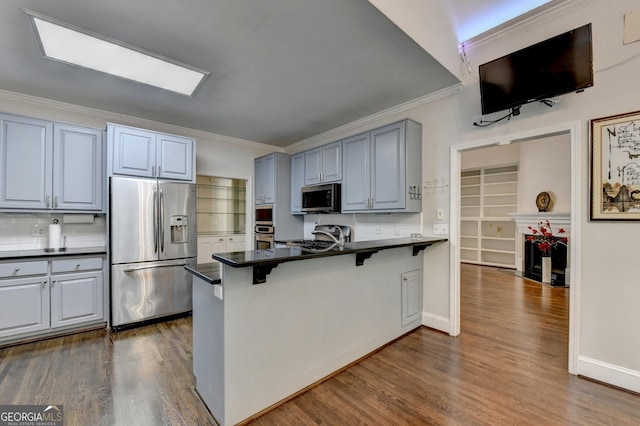 kitchen with a breakfast bar, a peninsula, dark wood finished floors, appliances with stainless steel finishes, and dark countertops