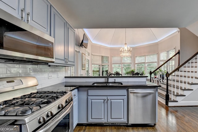kitchen with a peninsula, gray cabinetry, a sink, appliances with stainless steel finishes, and dark countertops