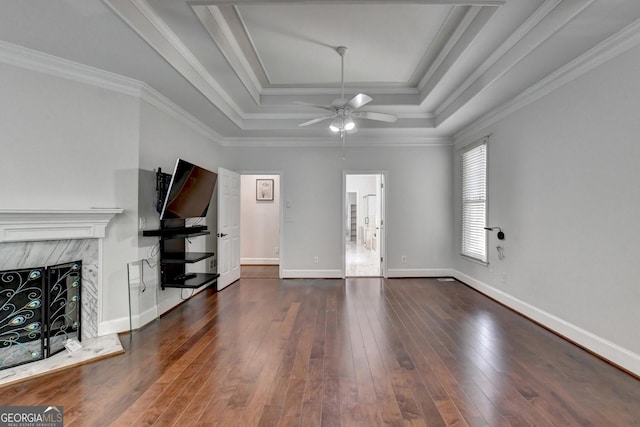unfurnished living room featuring a raised ceiling, ornamental molding, hardwood / wood-style floors, a fireplace, and baseboards