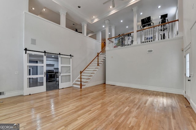 unfurnished living room featuring visible vents, stairs, a towering ceiling, and wood finished floors
