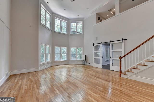 unfurnished living room with visible vents, stairs, a barn door, ornamental molding, and wood finished floors