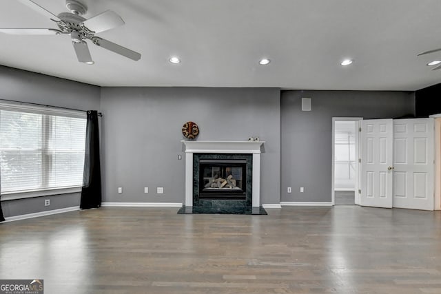 unfurnished living room featuring recessed lighting, a premium fireplace, baseboards, and wood finished floors
