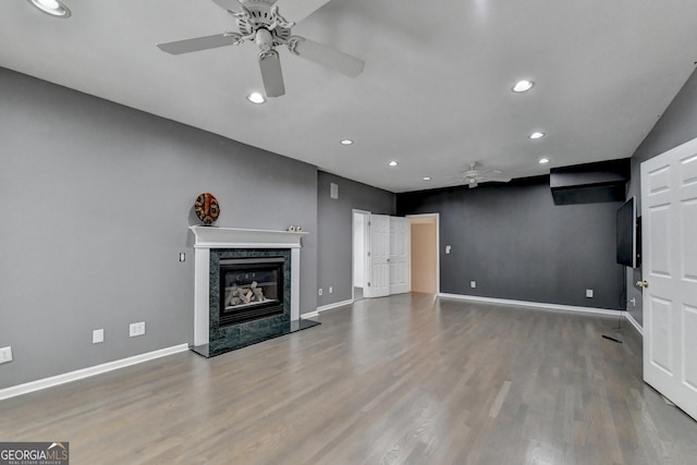 unfurnished living room featuring a high end fireplace, baseboards, a ceiling fan, and wood finished floors