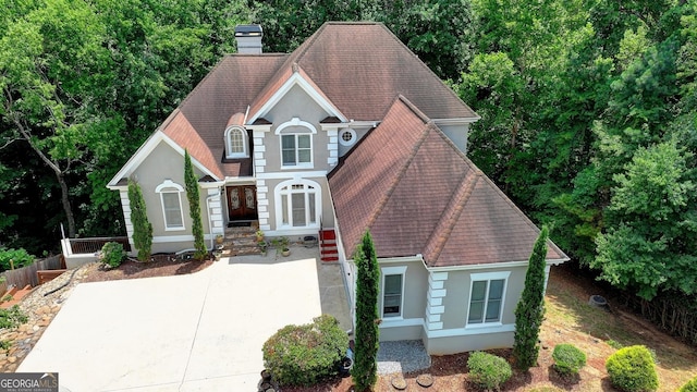 traditional-style house with stucco siding, driveway, a chimney, and a shingled roof