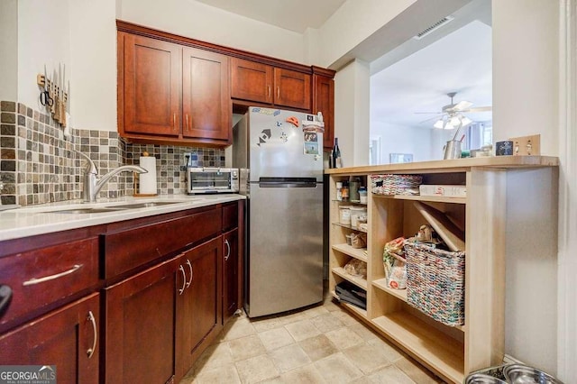 kitchen featuring visible vents, light countertops, decorative backsplash, freestanding refrigerator, and a sink