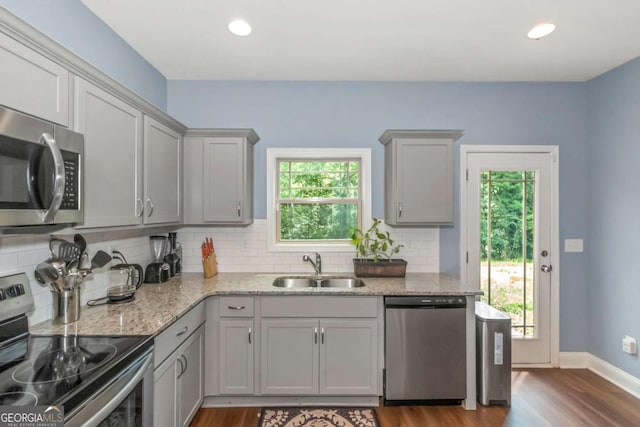 kitchen featuring wood finished floors, a sink, gray cabinetry, stainless steel appliances, and backsplash