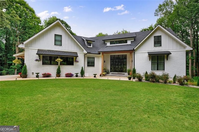 modern inspired farmhouse with brick siding, board and batten siding, a front lawn, and a shingled roof