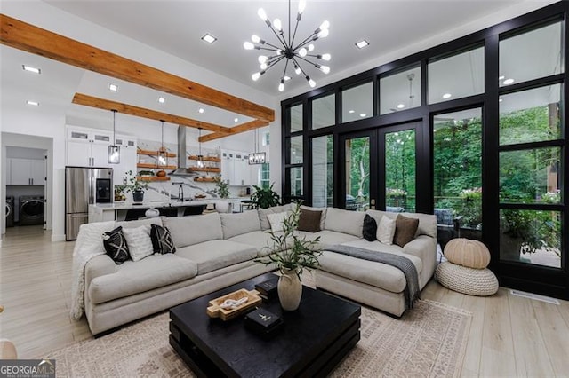 living area with light wood finished floors, an inviting chandelier, beam ceiling, separate washer and dryer, and a towering ceiling