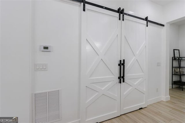 interior space with a barn door, wood finished floors, visible vents, and baseboards