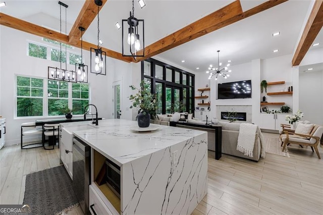 kitchen featuring a kitchen island with sink, beam ceiling, a notable chandelier, and a glass covered fireplace