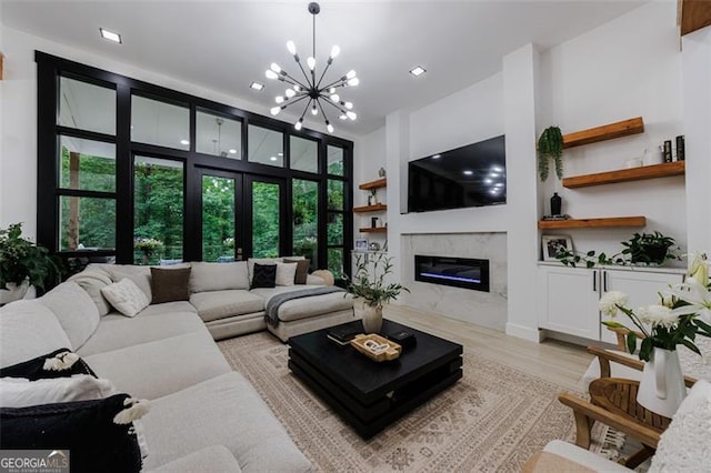 living room with an inviting chandelier, french doors, light wood-type flooring, and a premium fireplace