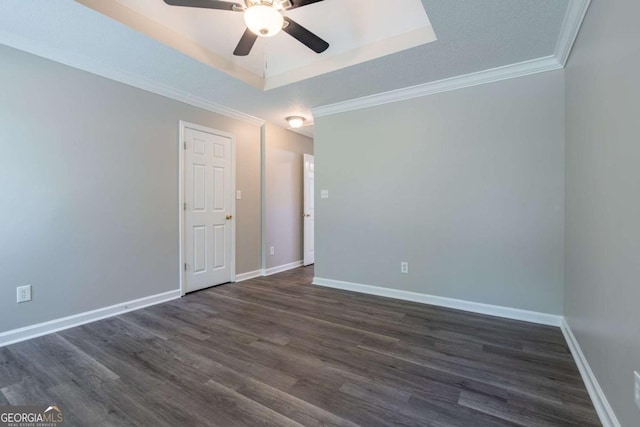 unfurnished room featuring a tray ceiling, dark wood-style floors, baseboards, and ornamental molding