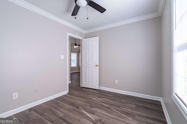 spare room with crown molding, baseboards, dark wood-style flooring, and a wealth of natural light