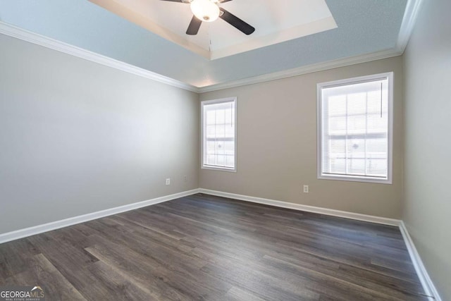 empty room with ornamental molding, a tray ceiling, baseboards, ceiling fan, and dark wood-style flooring