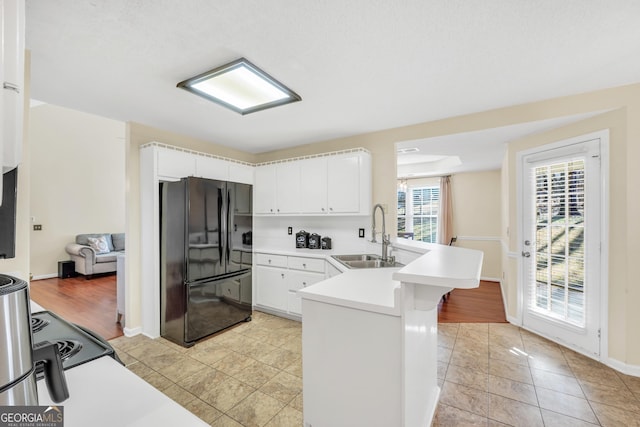 kitchen with light countertops, a peninsula, freestanding refrigerator, white cabinetry, and a sink