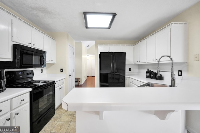 kitchen with a kitchen bar, black appliances, a peninsula, and a sink