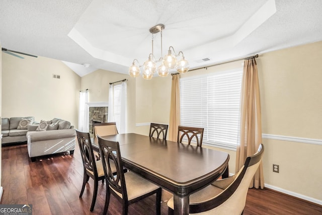 dining area featuring visible vents, a fireplace, a tray ceiling, and dark wood-style flooring