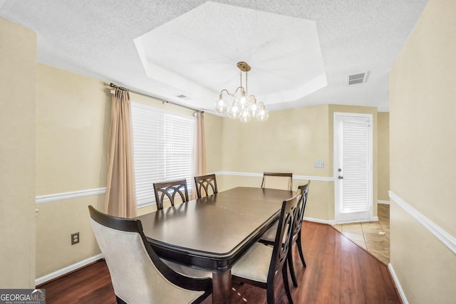 dining room with a tray ceiling, wood finished floors, visible vents, and a textured ceiling