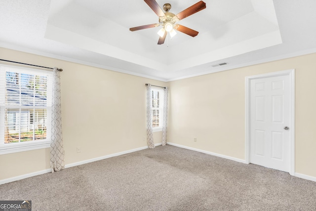 carpeted spare room with visible vents, a raised ceiling, and baseboards