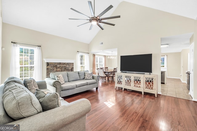 living area featuring visible vents, ceiling fan with notable chandelier, a stone fireplace, and wood finished floors