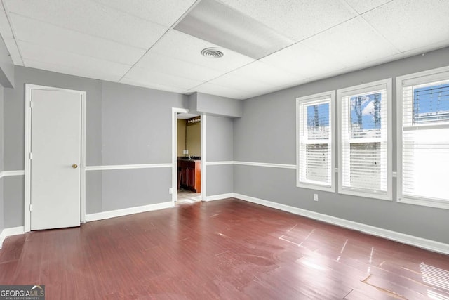 spare room featuring a drop ceiling, baseboards, visible vents, and wood finished floors