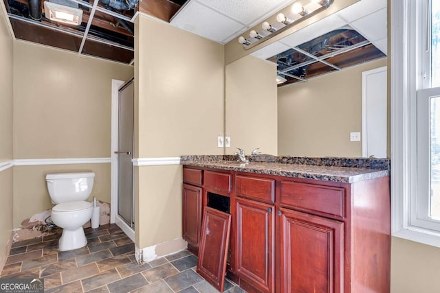 bathroom featuring vanity, baseboards, a shower stall, stone finish flooring, and toilet