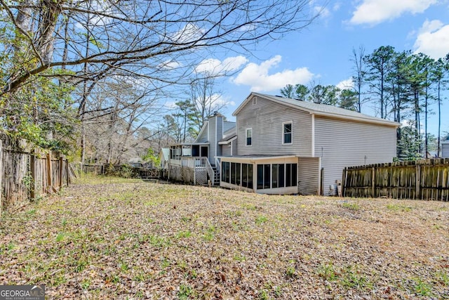 back of property featuring a chimney, a fenced backyard, and a sunroom