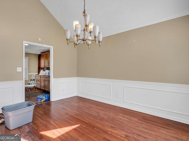 unfurnished room featuring a notable chandelier, a textured ceiling, wood finished floors, wainscoting, and vaulted ceiling