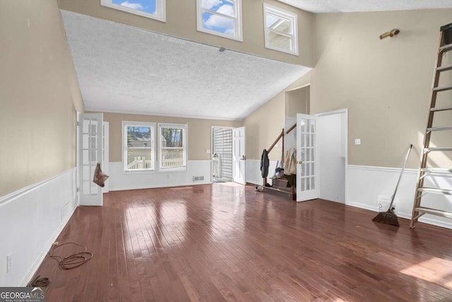 unfurnished living room featuring visible vents, stairs, hardwood / wood-style floors, wainscoting, and a textured ceiling