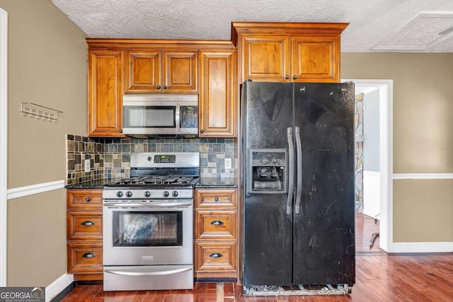 kitchen featuring dark countertops, dark wood finished floors, stainless steel appliances, brown cabinetry, and decorative backsplash