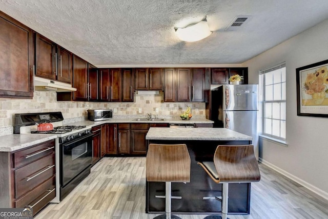 kitchen featuring under cabinet range hood, light countertops, decorative backsplash, appliances with stainless steel finishes, and a sink