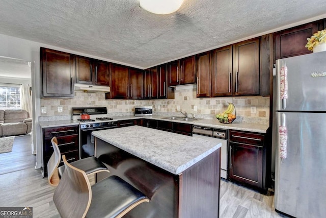 kitchen featuring light countertops, light wood finished floors, under cabinet range hood, and stainless steel appliances