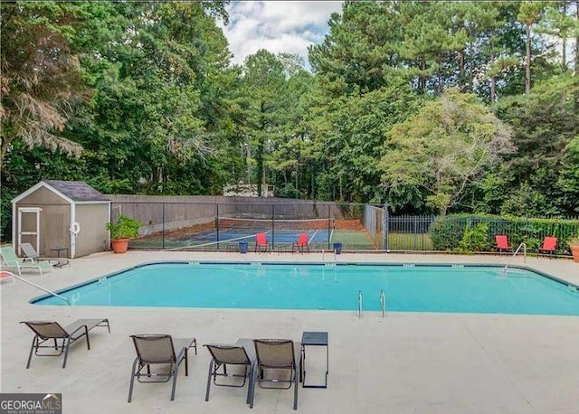 pool with a patio area, an outdoor structure, fence, and a shed