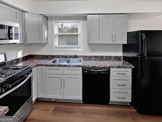 kitchen with a sink, black appliances, dark wood-style floors, and dark stone countertops