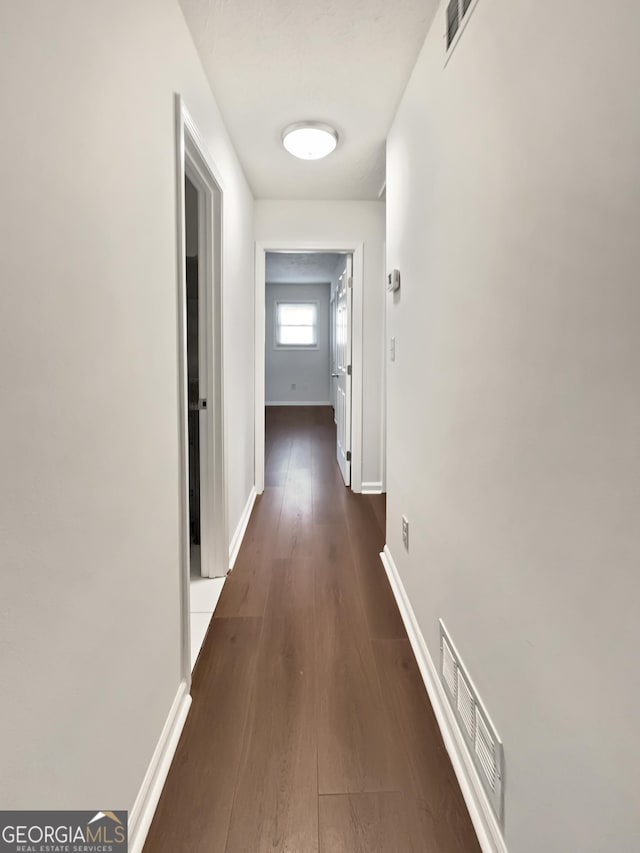 corridor with visible vents, baseboards, and dark wood-style floors