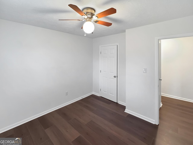 unfurnished bedroom with baseboards, a textured ceiling, dark wood-style floors, and a ceiling fan