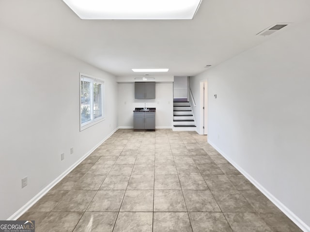 unfurnished living room with light tile patterned floors, visible vents, baseboards, and stairway