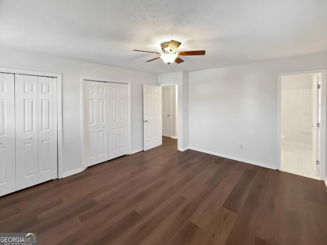 unfurnished bedroom with two closets, baseboards, and dark wood-style flooring