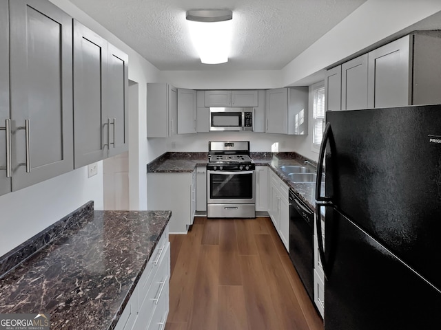 kitchen featuring dark wood finished floors, dark stone counters, gray cabinets, black appliances, and a sink