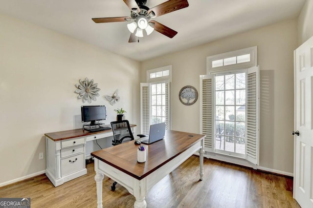 office featuring a healthy amount of sunlight, baseboards, light wood finished floors, and ceiling fan