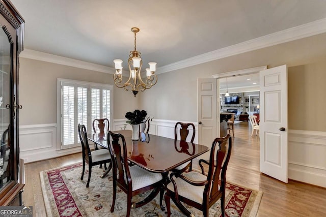 dining room with a fireplace, light wood-style floors, a wainscoted wall, and ornamental molding