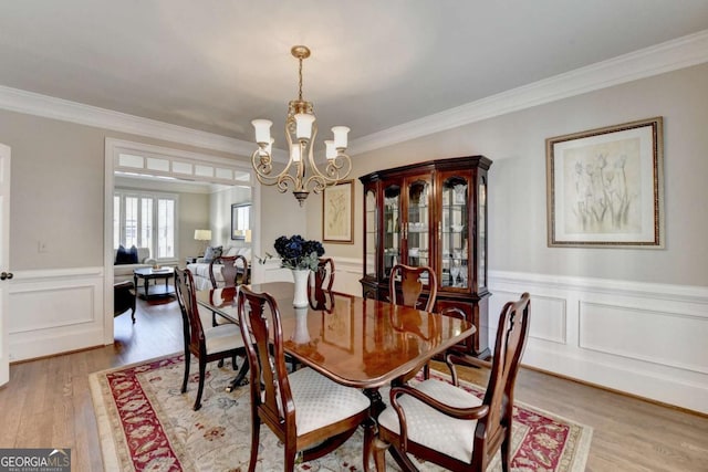 dining area featuring wainscoting, an inviting chandelier, light wood-style flooring, and crown molding