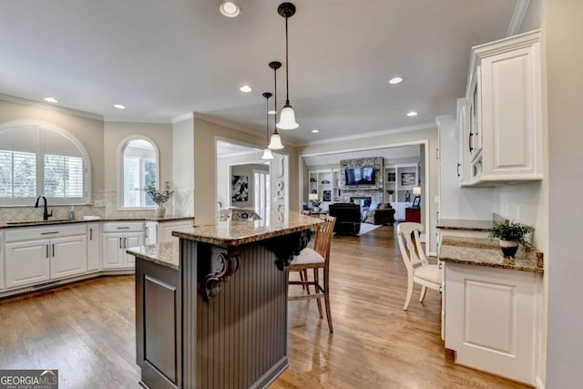 kitchen with open floor plan, a breakfast bar, light wood-type flooring, white cabinets, and a sink