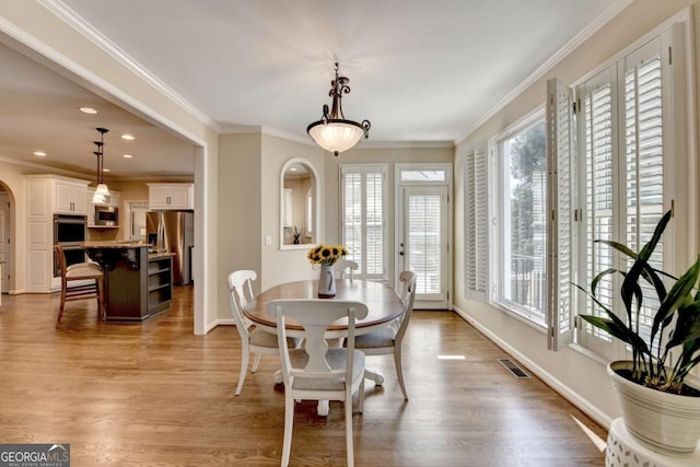 dining space featuring crown molding, plenty of natural light, wood finished floors, and arched walkways