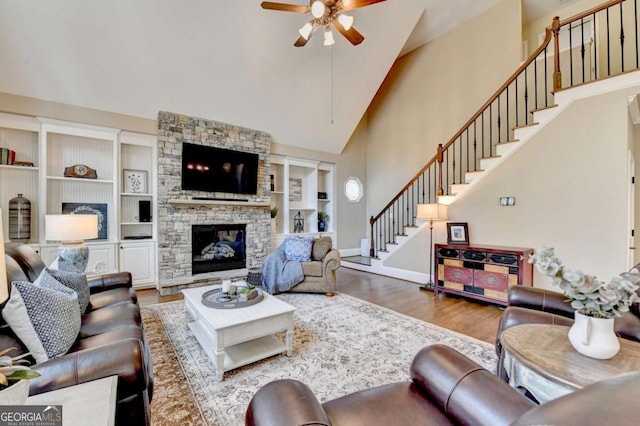 living area featuring stairway, a ceiling fan, wood finished floors, high vaulted ceiling, and a fireplace