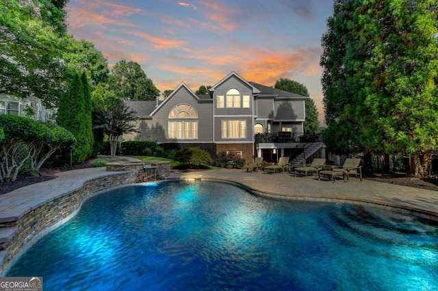 pool at dusk featuring stairway, an outdoor pool, and a patio