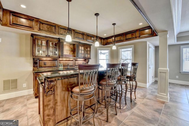 bar featuring hanging light fixtures, a healthy amount of sunlight, visible vents, and ornate columns