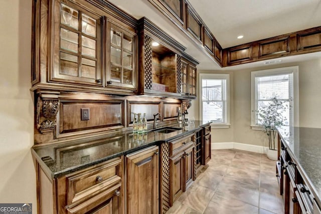 kitchen with dark stone counters, glass insert cabinets, baseboards, and a sink