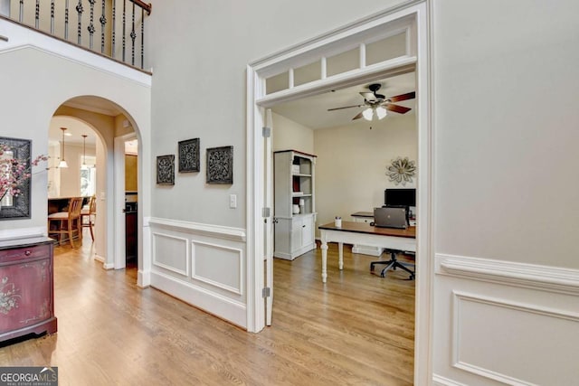 office with a ceiling fan, a wainscoted wall, arched walkways, a decorative wall, and light wood-type flooring